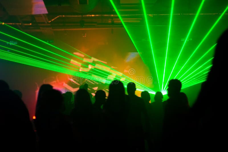 Silhouettes of dancing people in green laser lights at disco club