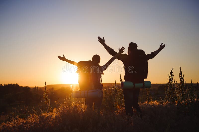 Silhouettes de deux randonneurs avec des sacs à dos marchant au coucher du soleil Trekking et apprécier la vue de coucher du sole photo stock Silhouettes de deux randonneurs avec des sacs à dos marchant au coucher du soleil Trekking et apprécier la vue de coucher du sole photo stock