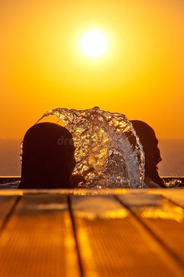 Silhouettes de filles de natation et eau d'éclaboussement contre la mer au su image stock Silhouettes de filles de natation et eau d'éclaboussement contre la mer au su image stock