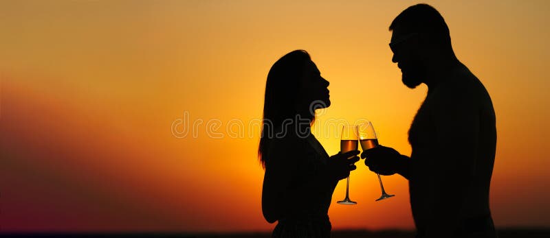 Silhouettes de l'homme et de la femme au fond dramatique de ciel de coucher du soleil, couple grillant des verres de vin dans l'a image libre de droits Silhouettes de l'homme et de la femme au fond dramatique de ciel de coucher du soleil, couple grillant des verres de vin dans l'a image libre de droits