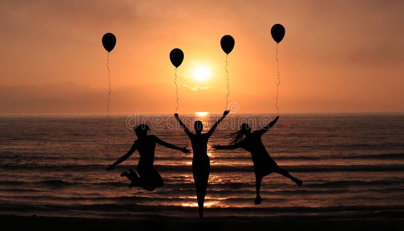 Silhouettes Of Happy Girls Jumping On the Sunset Beach Enjoying life Together With Party Balloons. Holidays and Happiness concept