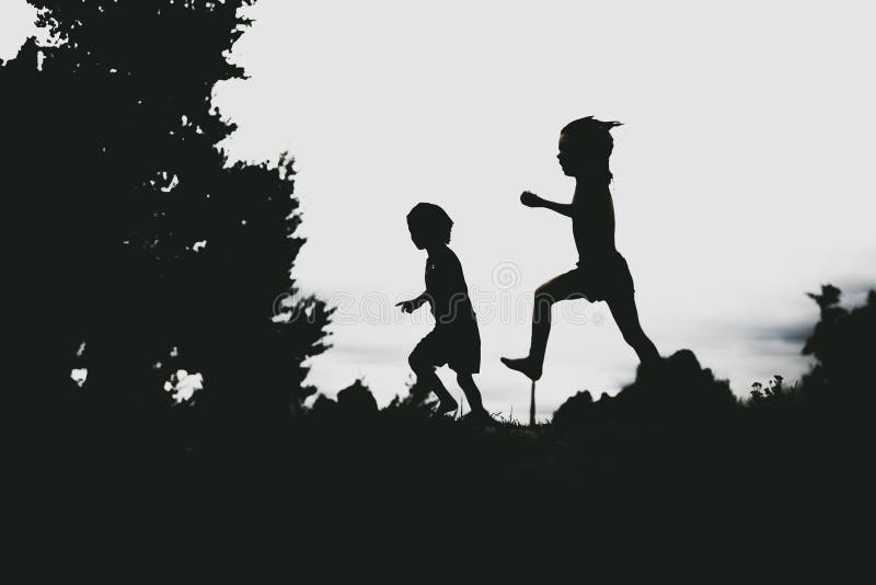 Silhouettes of kids jumping from a sand cliff at the beach. Active healthy kids enjoying their time at the beach. Fraternal twins playing together. Friends having fun during summer vacation. Nice day at the lake.