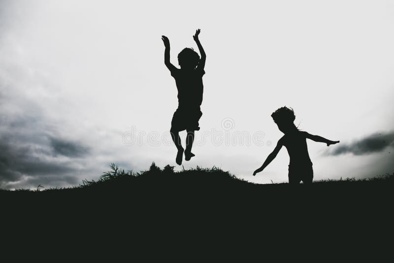 Silhouettes of kids jumping from a sand cliff at the beach. Active healthy kids enjoying their time at the beach. Fraternal twins playing together. Friends having fun during summer vacation. Nice day at the lake.