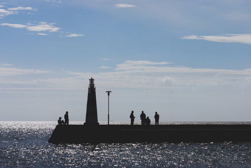 People at sea with a lighthouse in autumn stock photo People at sea with a lighthouse in autumn stock photo