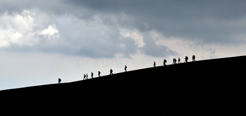 Silhouettes of tourists, walking downhill, on the horizon, dark background.