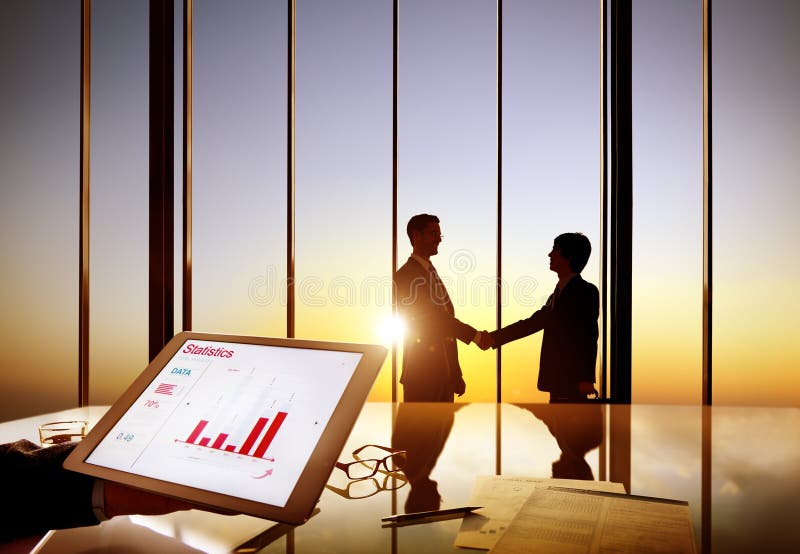 Silhouettes Of Two Businessmen Shaking Hands Together In A Board Room