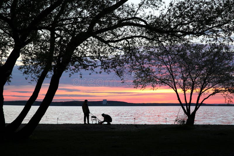 Silhouettes of two fishermen under large trees stock photography Silhouettes of two fishermen under large trees stock photography