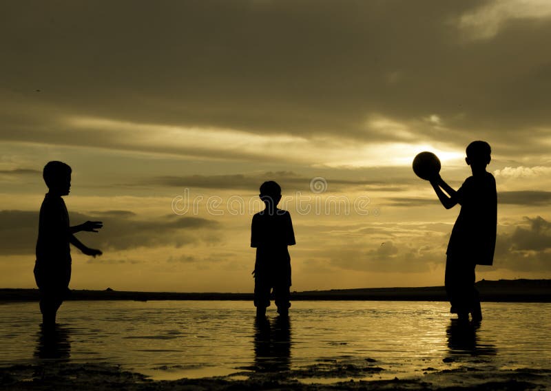 Silhouettez les garçons heureux d'image jouant le football de plage au temps d'aube avec le beau fond de lever de soleil photographie stock libre de droits