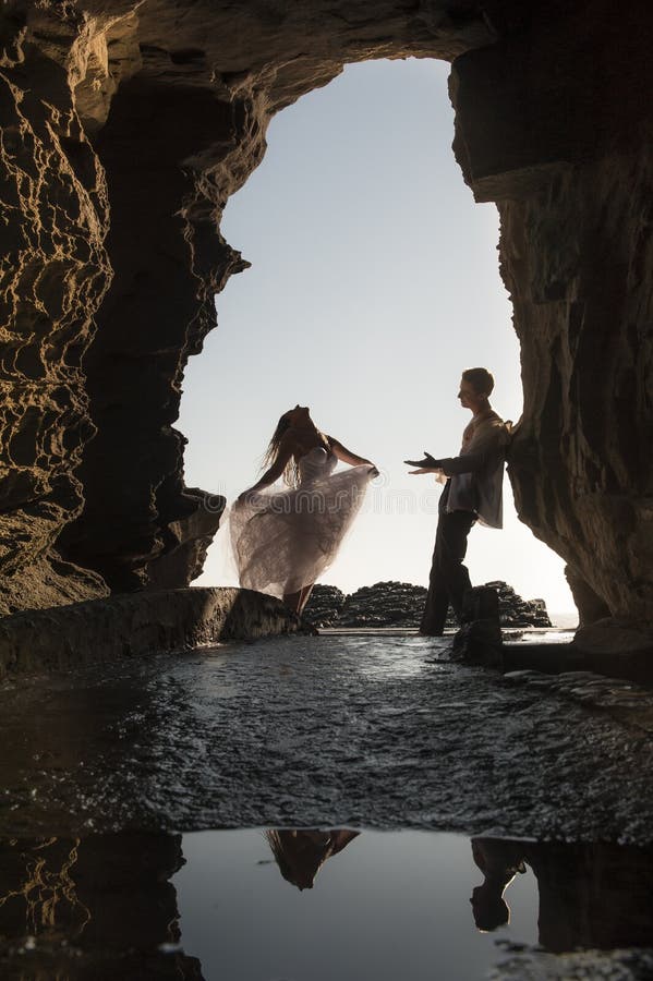 Silhouettez les jeunes beaux couples nuptiales dans l'arcade de roche à la plage photo stock Silhouettez les jeunes beaux couples nuptiales dans l'arcade de roche à la plage photo stock