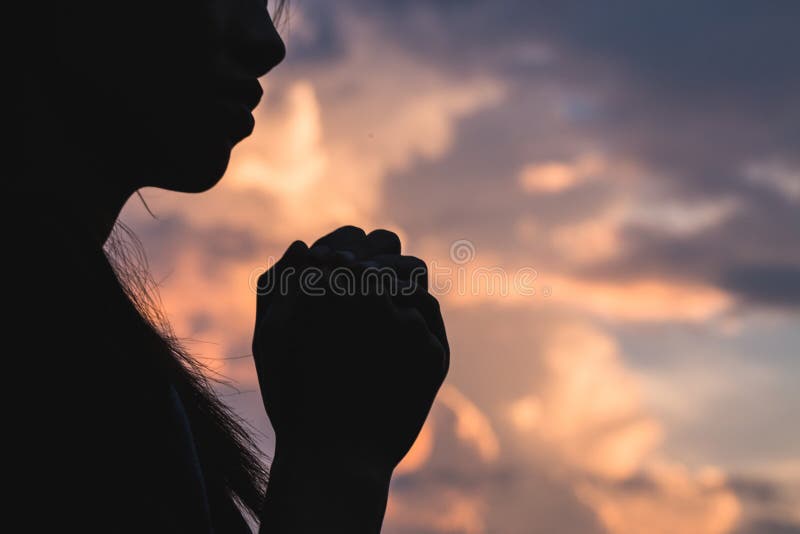 Silhouettieren Sie weg von der jungen Frau, die für Gott ` s Segen mit Th betet
