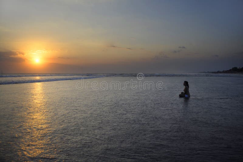 Silhueta da mulher asiática bonita nova que senta-se na água da areia livre e relaxado olhando o sol na praia do por do sol imagem de stock royalty free Silhueta da mulher asiática bonita nova que senta-se na água da areia livre e relaxado olhando o sol na praia do por do sol imagem de stock royalty free
