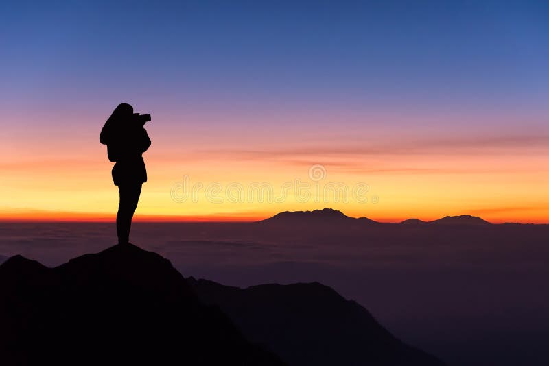 Silhueta da mulher que toma a fotografia na parte superior da montanha e imagens de stock Silhueta da mulher que toma a fotografia na parte superior da montanha e imagens de stock