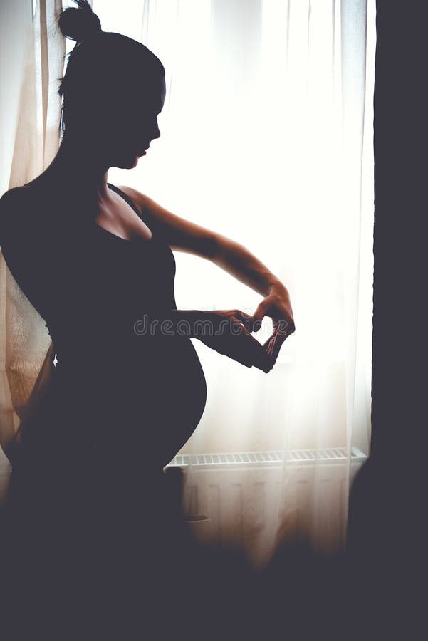 Silhueta da mãe bonita Retrato da mulher gravida feliz, sorrindo que faz um coração foto de stock Silhueta da mãe bonita Retrato da mulher gravida feliz, sorrindo que faz um coração foto de stock