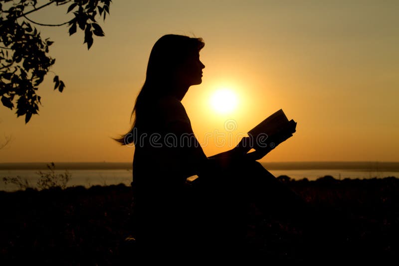 Silhueta De Uma Menina Com Um Livro No Por Do Sol Foto de Stock - Imagem de  livro, menina: 57062634