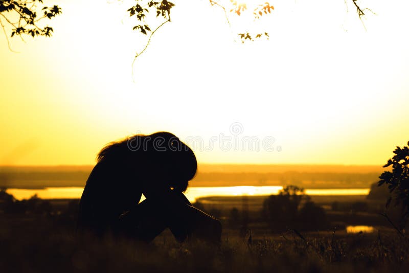 silhueta de mulher triste com a cabeça de joelhos ao pôr do sol