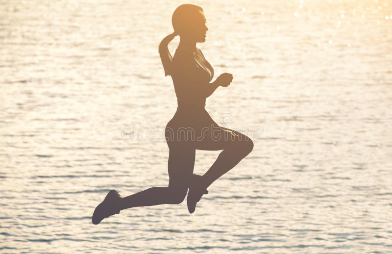 Silhueta de uma menina magro bonita que salte em um fundo de um por do sol na praia fotografia de stock Silhueta de uma menina magro bonita que salte em um fundo de um por do sol na praia fotografia de stock