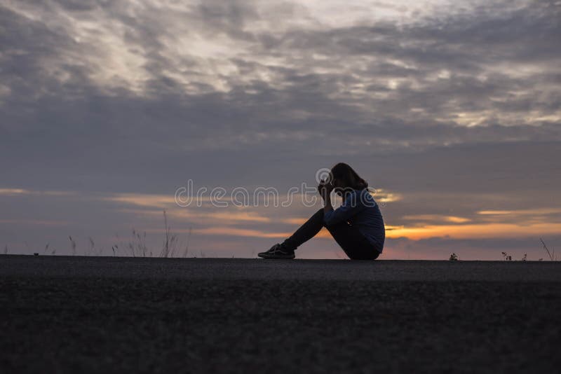silhueta de mulher triste com a cabeça de joelhos ao pôr do sol