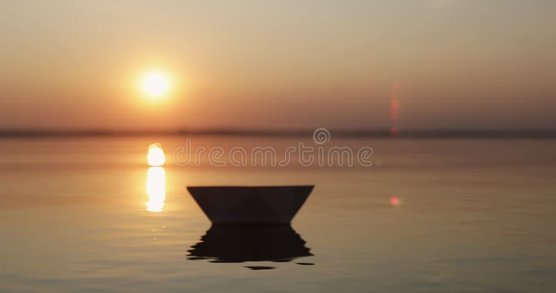 Silhueta de uma mão humana que solta um barco de papel em água do mar ou lago ao pôr do sol. t