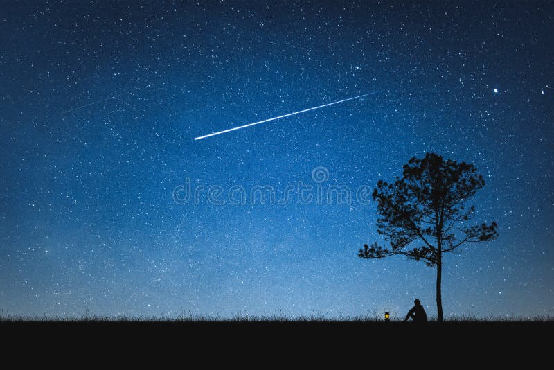 Silhueta do homem que senta-se na montanha e no céu noturno com estrela de tiro conceito sozinho