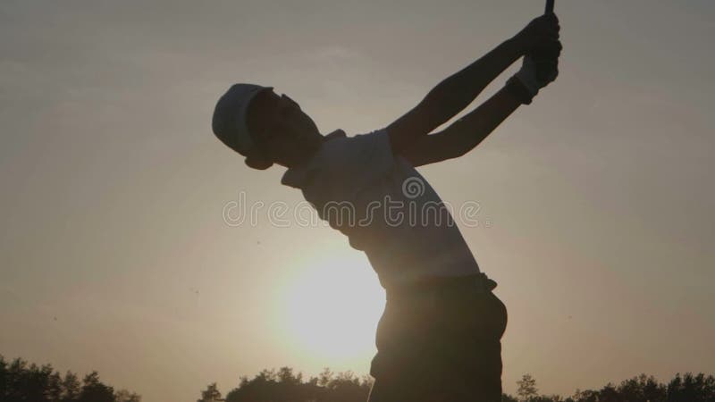 Silhueta do jogador de golfe do menino com o saco de golfe no por do sol