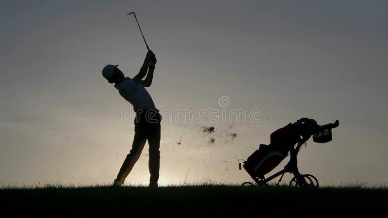 Silhueta do jogador de golfe do menino com o saco de golfe no por do sol