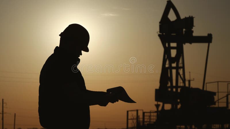 Silhuetas do coordenador na bomba da plataforma petrolífera da indústria petroquímica no céu do por do sol O suporte do trabalhad