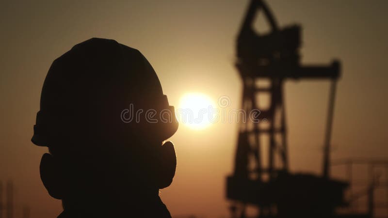 Silhuetas do coordenador na bomba da plataforma petrolífera da indústria petroquímica no céu do por do sol O suporte do trabalhad