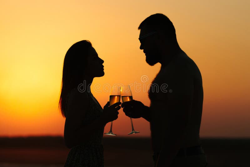 Silhuetas do homem e da mulher, par feliz no amor na praia no por do sol, olhando-se, sorrindo e realizando em seu ha imagens de stock Silhuetas do homem e da mulher, par feliz no amor na praia no por do sol, olhando-se, sorrindo e realizando em seu ha imagens de stock