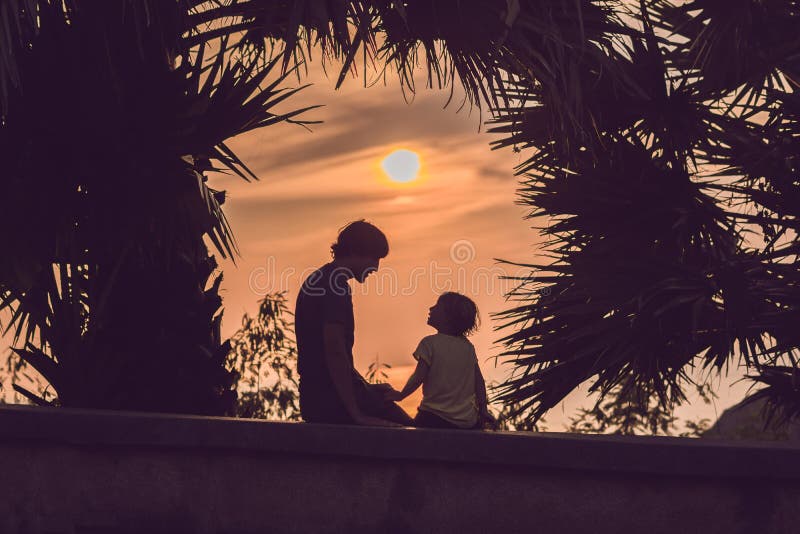 Silhuetas do pai e do filho, que encontram o por do sol nos trópicos contra o contexto das palmeiras fotografia de stock royalty free Silhuetas do pai e do filho, que encontram o por do sol nos trópicos contra o contexto das palmeiras fotografia de stock royalty free