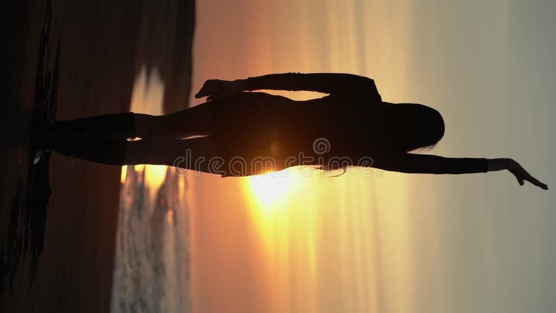 Silhueterkvinna med händer upphöjda stående sandstrand vid soluppgång. långsam rörelse lodrätt