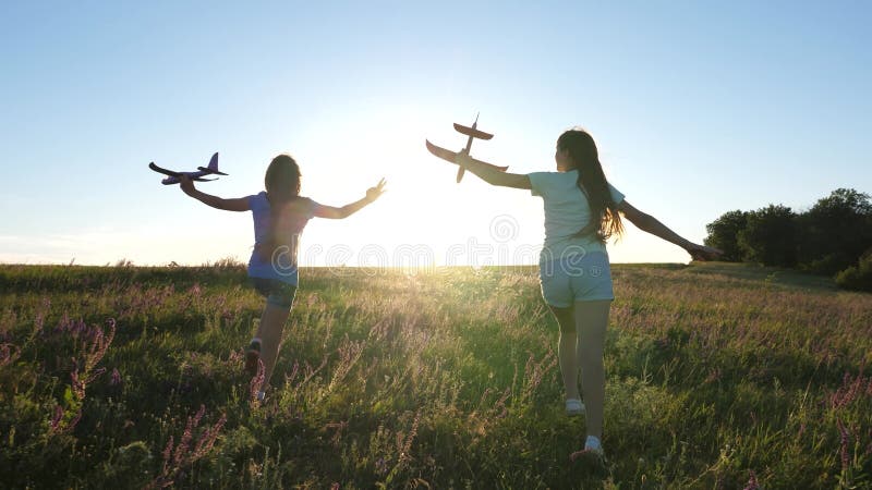 Silhuett av barn som leker på ett flygplan på ett blomfält. drömmar om flygning. lycklig barndom. två flickor leker med