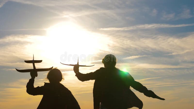 Silhuett av barn som leker på planet. Barn framför himlen och solen med ett flygplan i handen.. drömmar om