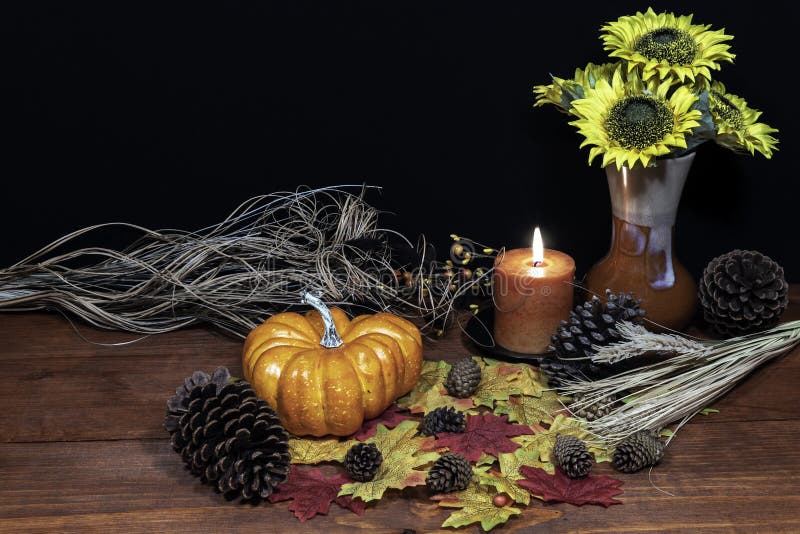 Silk maple leaves, beautiful bouquet of sunflowers, frosted pine cones and orange candle on tabletop with dark background.