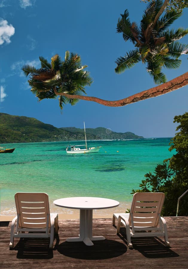 Deck chairs is waiting in front of the tropical beach. Palm trees , beach, beautiful sea with boats and blue sky as background. The sky area is free for your text. Deck chairs is waiting in front of the tropical beach. Palm trees , beach, beautiful sea with boats and blue sky as background. The sky area is free for your text.