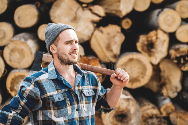 Silny brodaty lumberjack jest ubranym szkockiej kraty koszula chwyta ax w ręce na tle tartak zdjęcie royalty free Silny brodaty lumberjack jest ubranym szkockiej kraty koszula chwyta ax w ręce na tle tartak zdjęcie royalty free