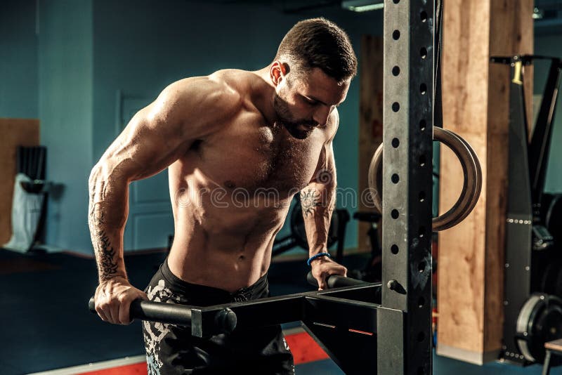 Silny mięśniowy mężczyzna robi Ups na nierównych barach w crossfit gym