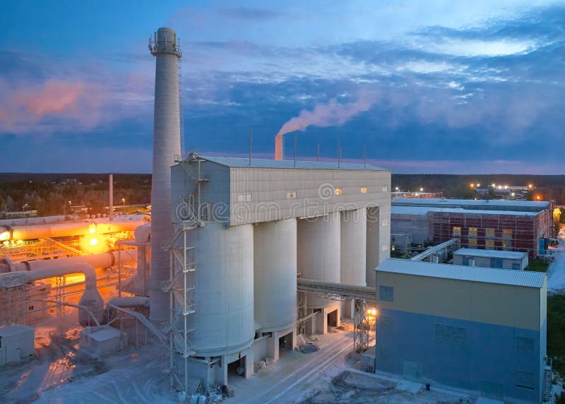 Silo towers for calx materials keeping at silica bricks production plant at night aerial view. Factory equipment against cloudy sky. Silo towers for calx materials keeping at silica bricks production plant at night aerial view. Factory equipment against cloudy sky