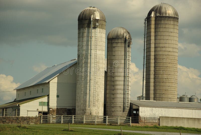 This is a shot of a white barn and 3 silos.