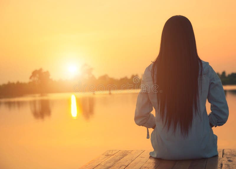 Silueta de la mujer joven relajante en el embarcadero de madera en el lago en puesta del sol imágenes de archivo libres de regalías Silueta de la mujer joven relajante en el embarcadero de madera en el lago en puesta del sol imágenes de archivo libres de regalías