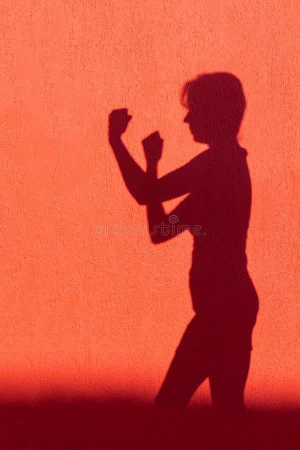 Silhouette of shadow projected by woman showing fists on red wall. Silhouette of shadow projected by woman showing fists on red wall