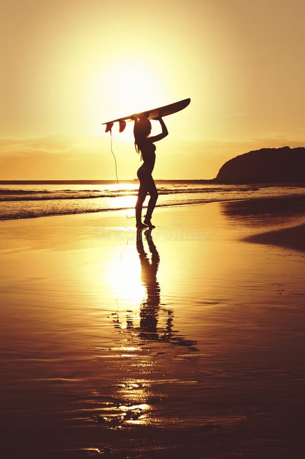 Silueta de la persona que practica surf que se coloca con el tablero de resaca en la playa fotografía de archivo libre de regalías Silueta de la persona que practica surf que se coloca con el tablero de resaca en la playa fotografía de archivo libre de regalías