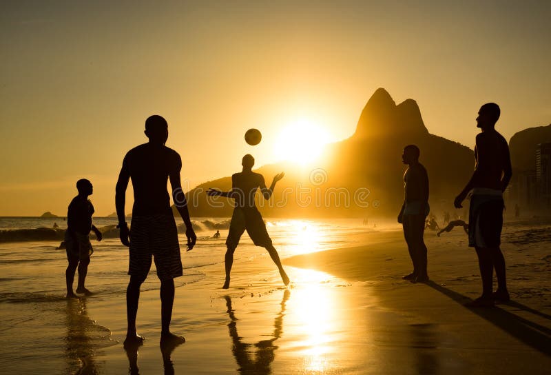 Silueta de los locals que juegan la bola en la puesta del sol en la playa de Ipanema, Rio de Janeiro, el Brasil