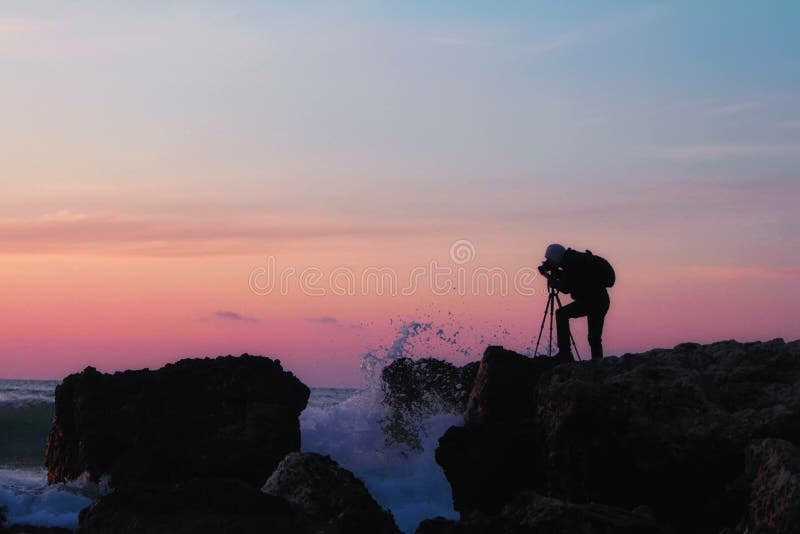Silueta de un fotógrafo con una mochila y un trípode con una puesta del sol hermosa del mar imagenes de archivo Silueta de un fotógrafo con una mochila y un trípode con una puesta del sol hermosa del mar imagenes de archivo