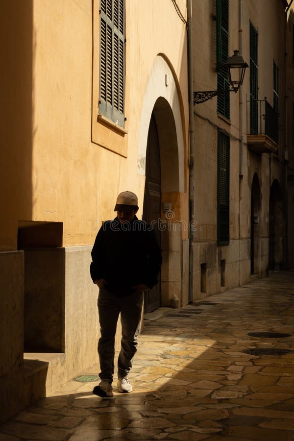 Silueta de un hombre que camina por una callejuela oscura en el centro de Palma de Mallorca iluminada por el sol fotos de archivo libres de regalías