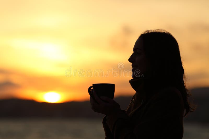 Silueta de una mujer sosteniendo una taza de café al atardecer en la playa fotografía de archivo