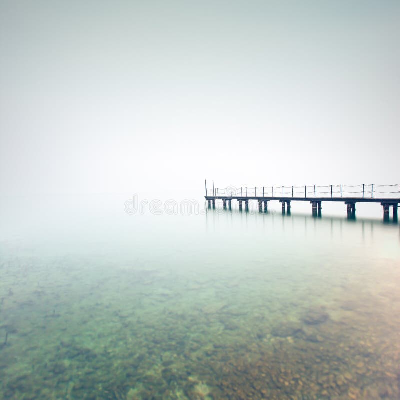 Pier or jetty silhouette in a foggy lake. Garda lake, Italy, Europe. Pier or jetty silhouette in a foggy lake. Garda lake, Italy, Europe