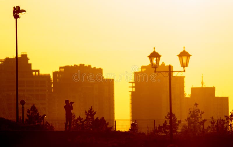Silueta del fotógrafo en el fondo de edificios hermosos en la ciudad en la puesta del sol imagenes de archivo Silueta del fotógrafo en el fondo de edificios hermosos en la ciudad en la puesta del sol imagenes de archivo