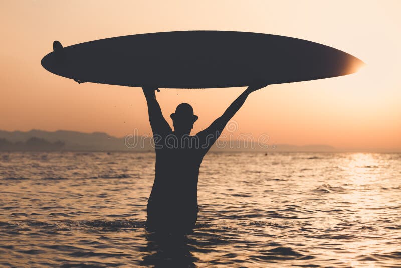 Silueta del hombre que sostiene la tabla hawaiana en la puesta del sol sobre el mar foto de archivo Silueta del hombre que sostiene la tabla hawaiana en la puesta del sol sobre el mar foto de archivo