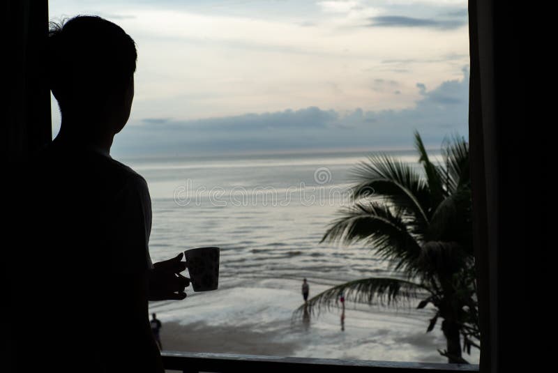 Silueta del hombre que sostiene la taza de café y que mira el mar imágenes de archivo libres de regalías