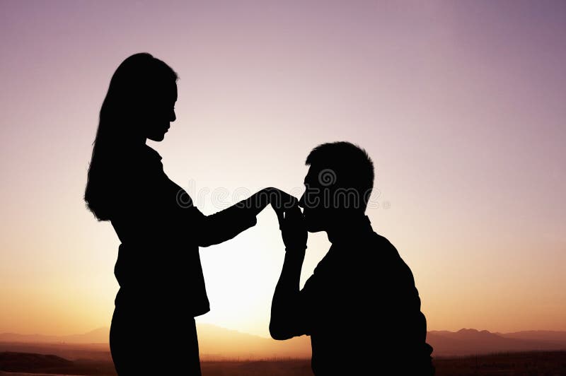 Silueta del novio que se arrodilla y que se besa la mano de las novias en la puesta del sol